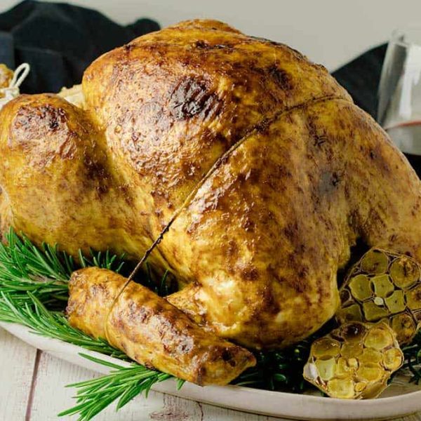 A white oval platter with a roasted turkey resting on a bed of rosemary sprigs
