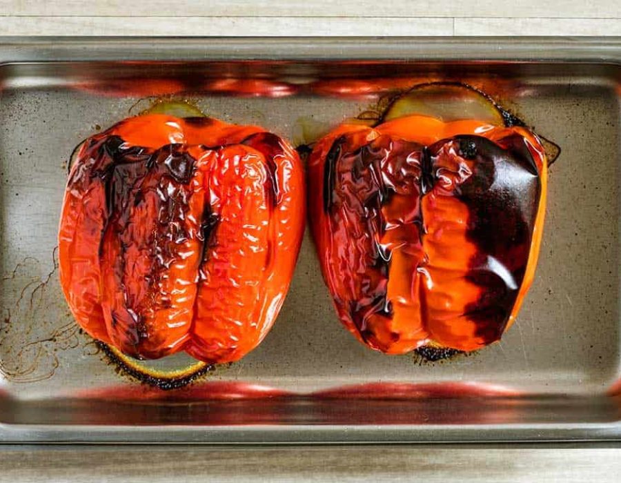 A silver baking tray with two whole roasted peppers
