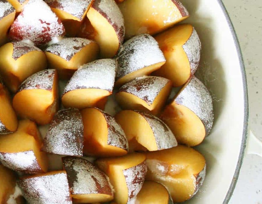 a white baking dish filled with sliced plums arranged standing up dusted with sugar