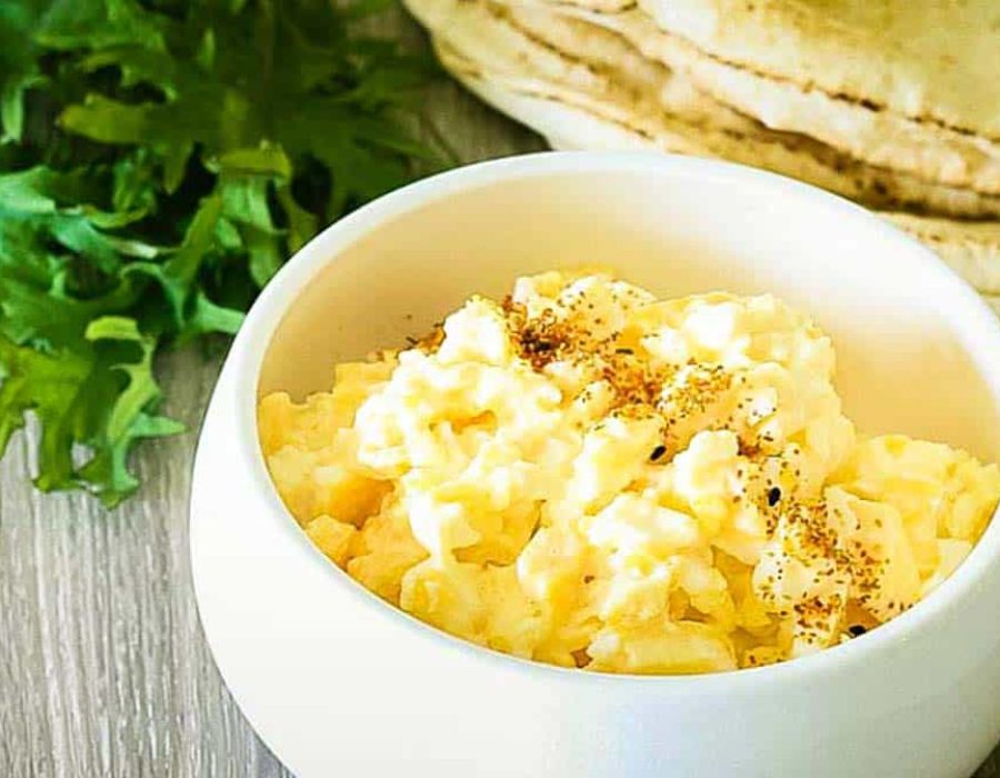 A small white bowl with fluffy, seasoned scrambled eggs with tortillas and rocket in the background.