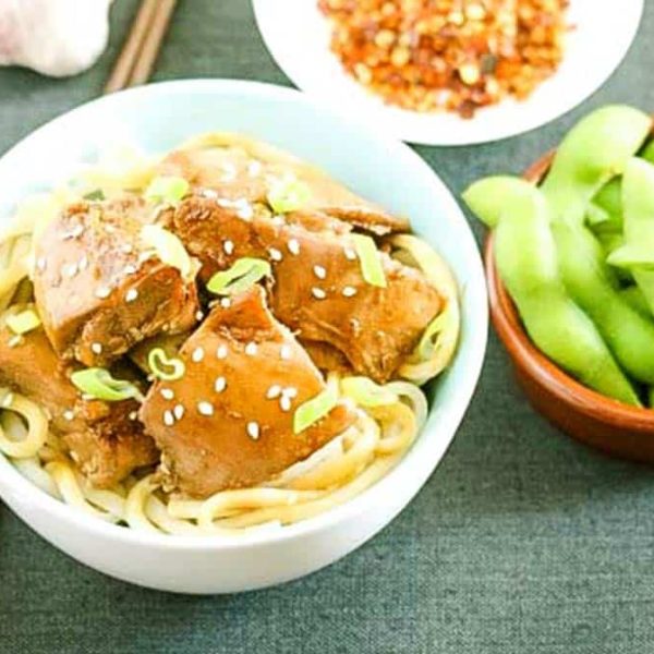 A bowl of noodles with chicken pieces and a bowl of edamame beans
