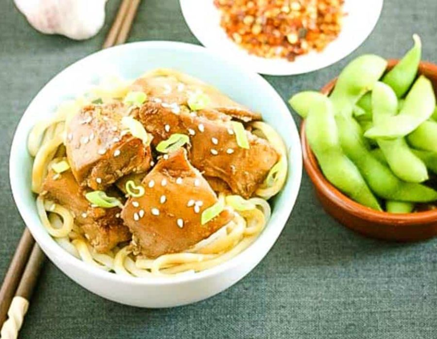 A bowl of noodles with chicken pieces and a bowl of edamame beans
