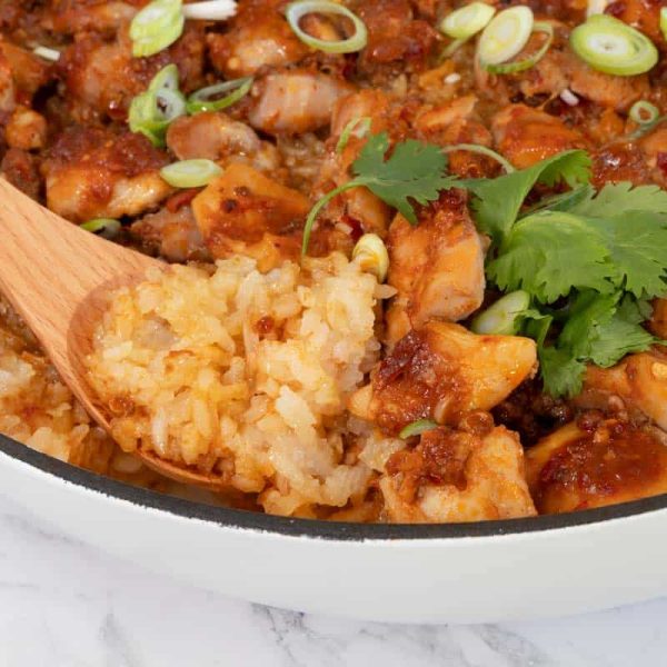 Wooden spoon scoops up a portion of cooked glutinous rice and marinated chicken from a white pan