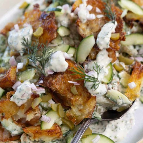 A top down view of smashed potato salad, with crispy roasted potatoes, herbs, vegetables and a creamy dressing.