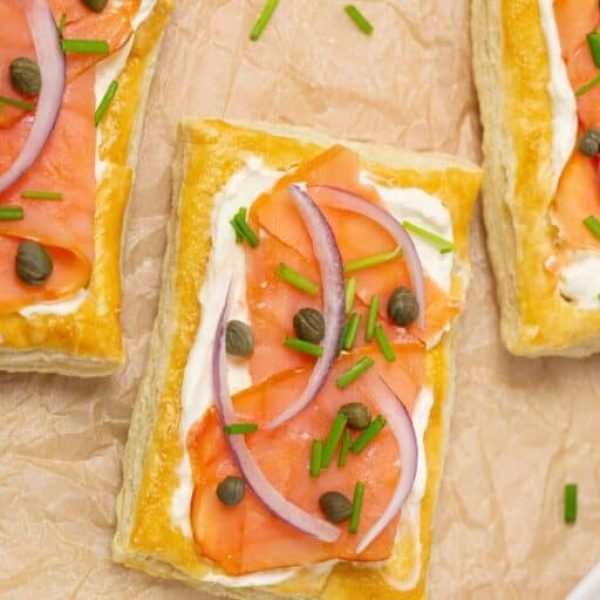 Three rectangular smoked salmon and cream cheese puff pastries arranged on brown parchment paper, for an article about Christmas puff pastry appetizers.