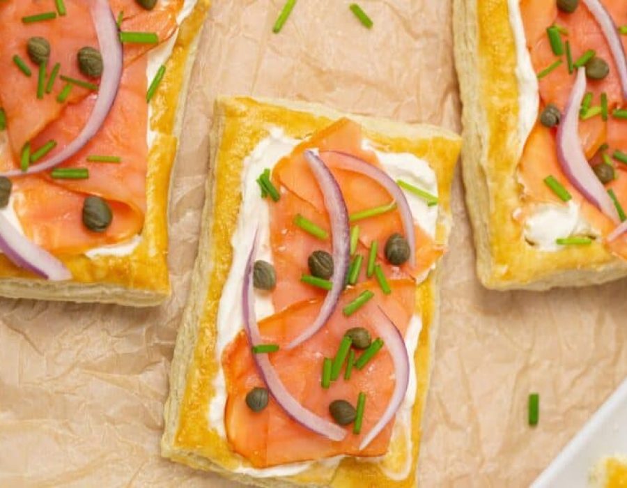 Three rectangular smoked salmon and cream cheese puff pastries arranged on brown parchment paper, for an article about Christmas puff pastry appetizers.