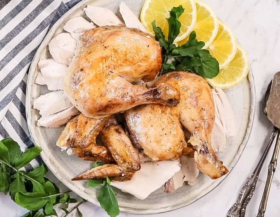 A sous vide roasted spatchcock chicken, carved and served on a white platter with lemon slices and fresh parsley on top.