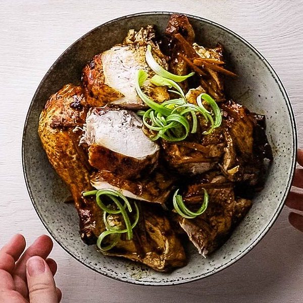 An overhead image of a serving dish with a whole chicken cut into pieces and garnished with spring onion curls
