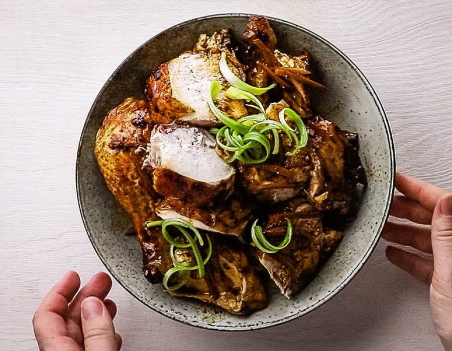 An overhead image of a serving dish with a whole chicken cut into pieces and garnished with spring onion curls