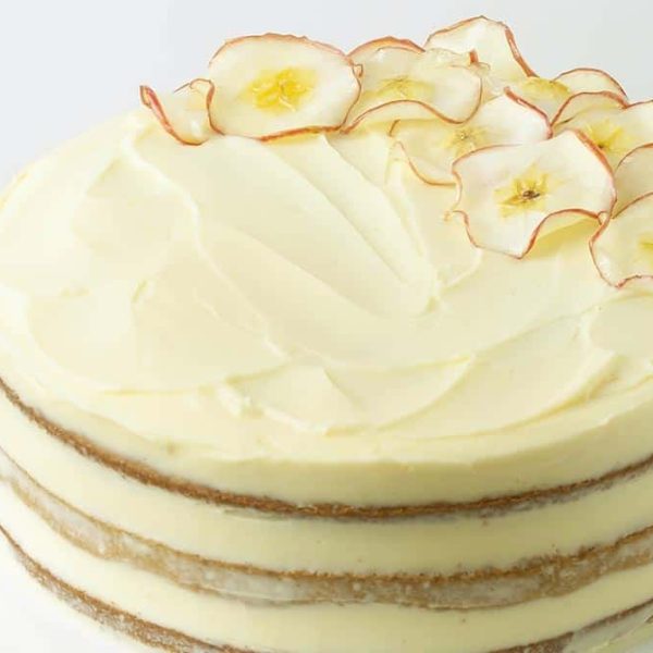 Spice Cake 1080×675 Web a triple layered apple spice cake with pale yellow frosting and decorative apple slices