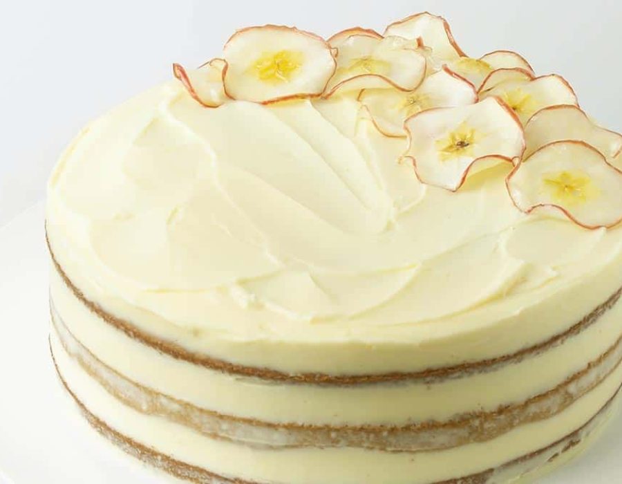 a triple layered apple spice cake with pale yellow frosting and decorative apple slices