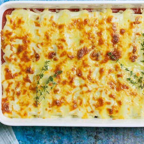 A white, rectangular casserole dish with cheesy topped baked cannelloni garnished with sprigs of thyme