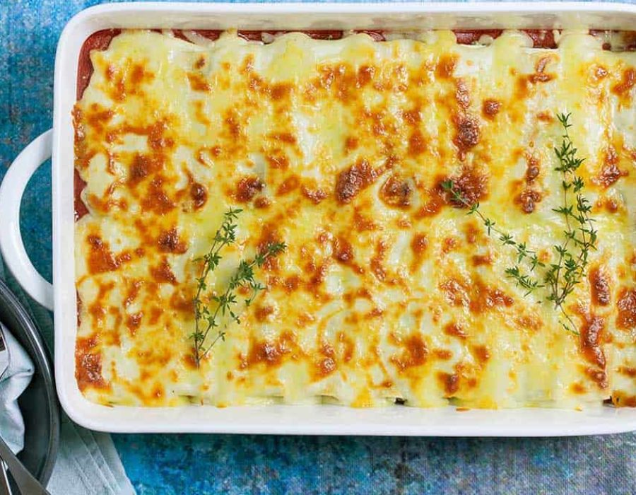 A white, rectangular casserole dish with cheesy topped baked cannelloni garnished with sprigs of thyme