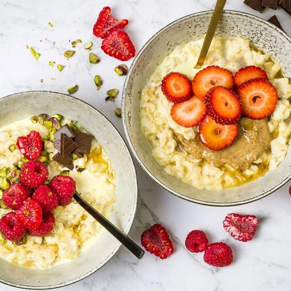 Two speckled bowls with oatmeal garnished with nuts, berries and chocolate
