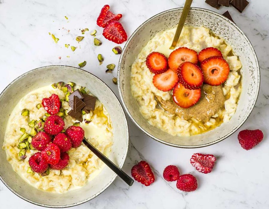 Two speckled bowls with oatmeal garnished with nuts, berries and chocolate