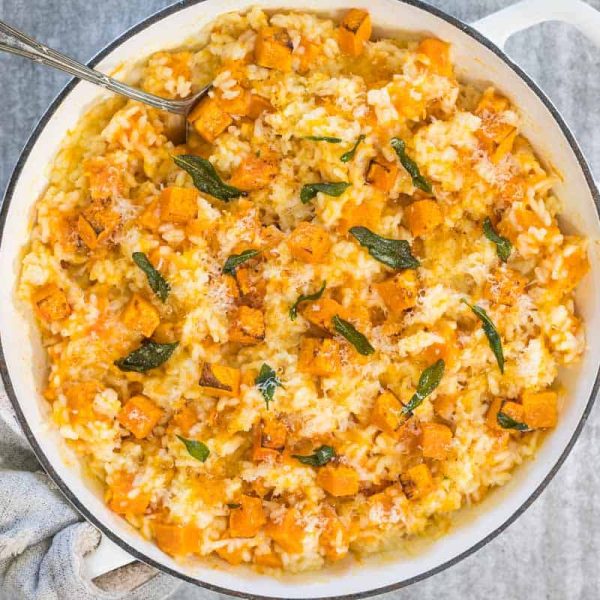 Steamed-Pumpkin-Risotto-14 Pumpkin and crispy sage steamed risotto, served in a white pan and viewed from above. A gray cloth is wrapped around one handle of the pan and a silver spoon rests in the dish.