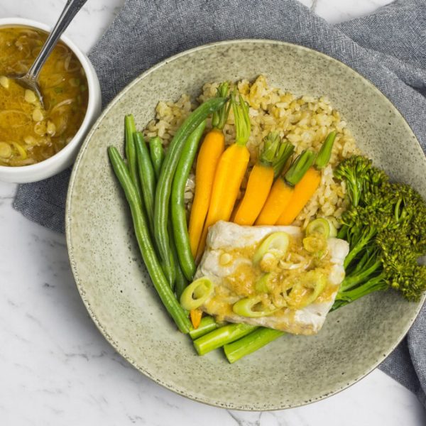 A zoomed out picture of a grey speckled plate with steamed fish, mixed vegetables with a bowl of miso dressing
