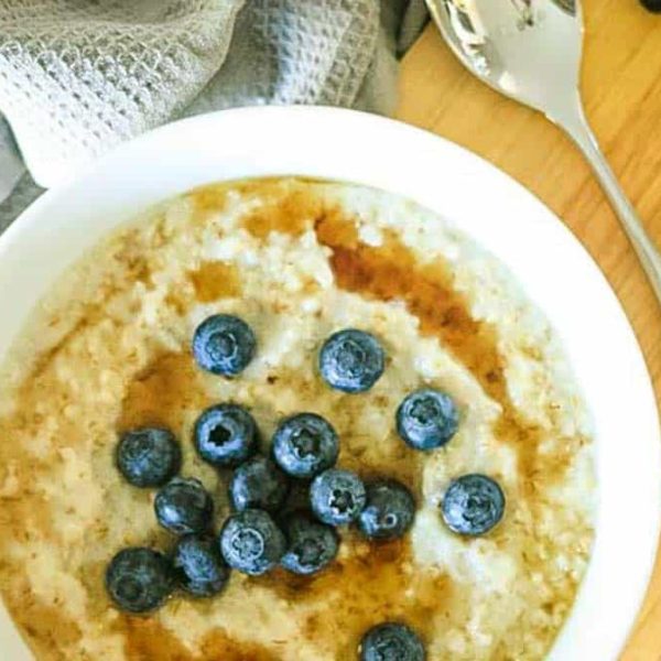 a bowl of porridge topped with syrup and blueberries on a wooden board