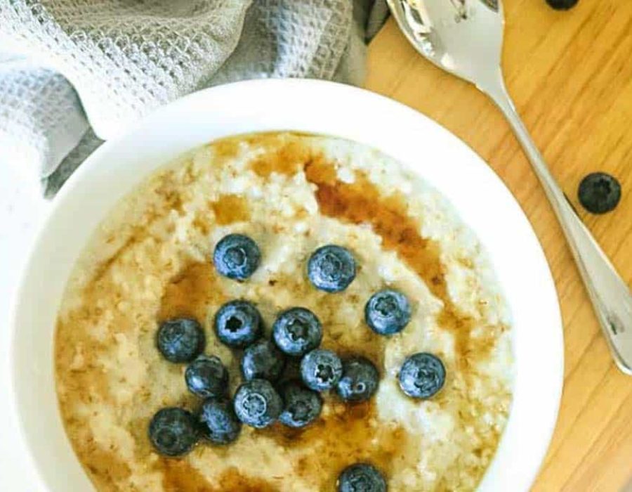 a bowl of porridge topped with syrup and blueberries on a wooden board