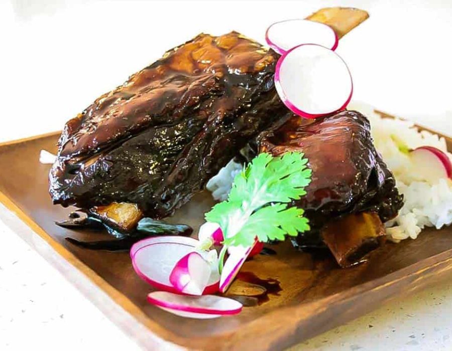 Sticky Asian Beef Ribs on a wooden plate with a serving of rice and garnishes.