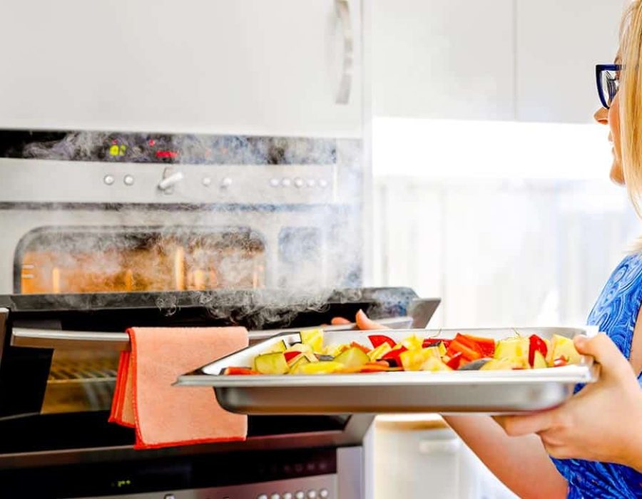 woman putting vegetables into steam oven