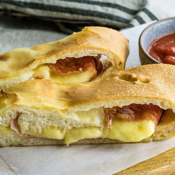 Two thick slices of meat and cheese filled stromboli on a board with a ramekin of sauce