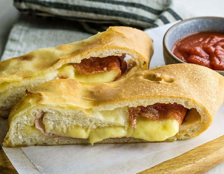 Two thick slices of meat and cheese filled stromboli on a board with a ramekin of sauce