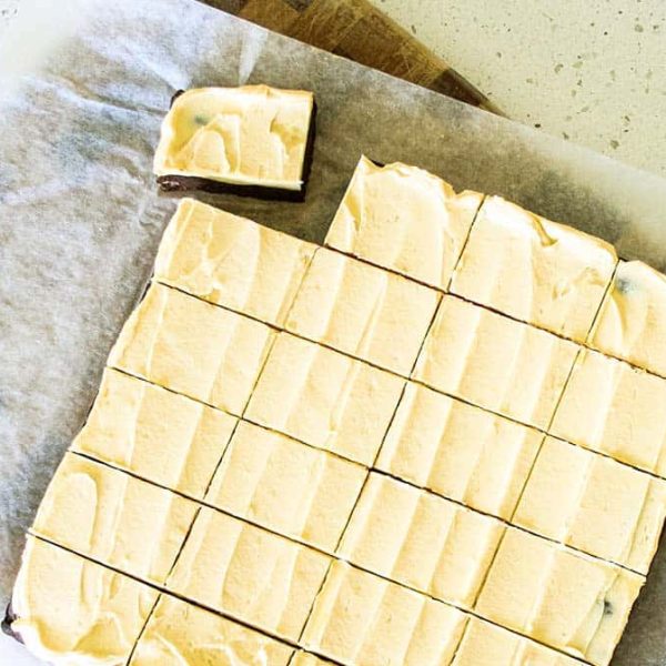A batch of frosted brownies cut into squares on a baking paper lined cutting board