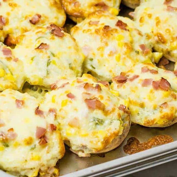 a stainless steel pan full of twice baked potatoes covered in melted cheese, bacon and scallions