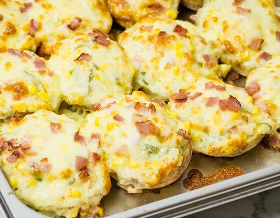 a stainless steel pan full of twice baked potatoes covered in melted cheese, bacon and scallions