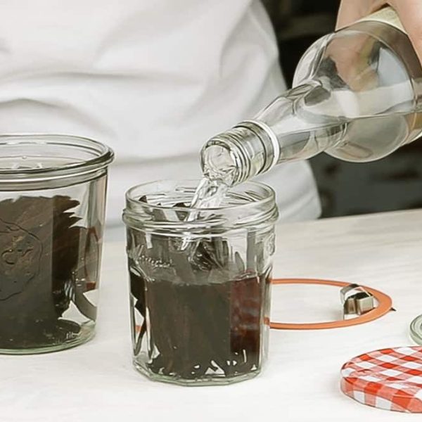 vodka being poured into a jar of vanilla beans