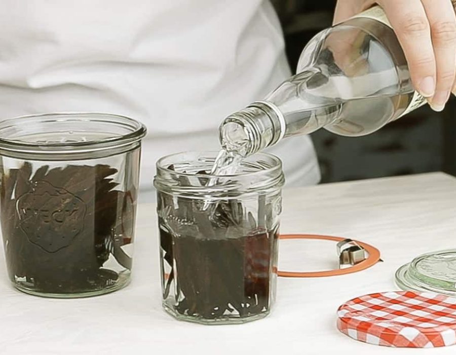 vodka being poured into a jar of vanilla beans