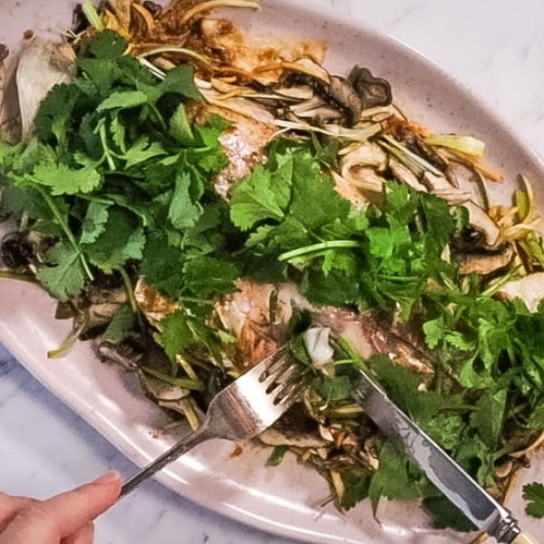 atop the marble counter is a white oval dish plate with Vietnamese steamed fish topped with cilantro