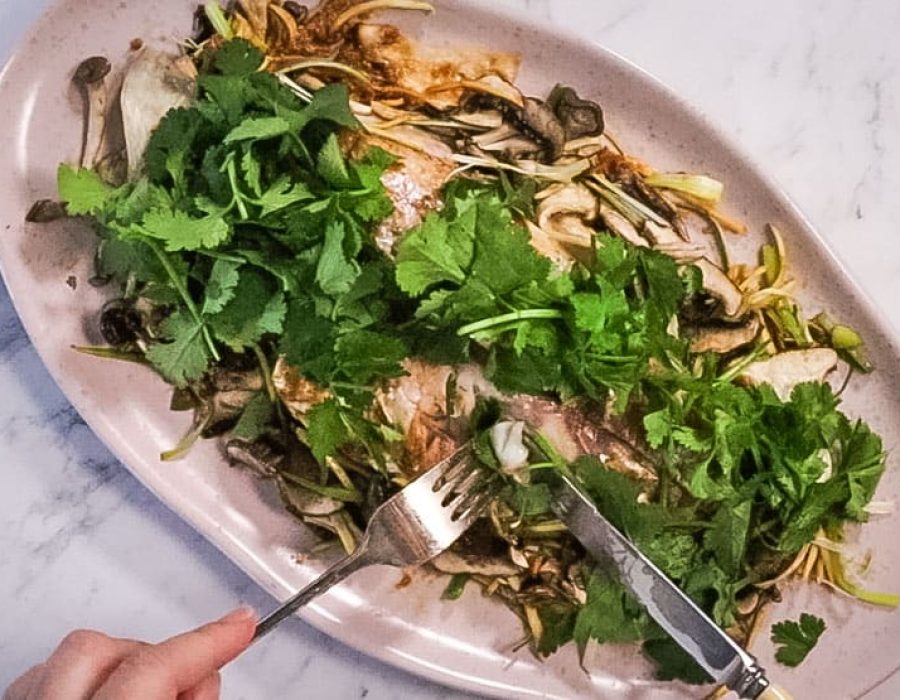 atop the marble counter is a white oval dish plate with Vietnamese steamed fish topped with cilantro